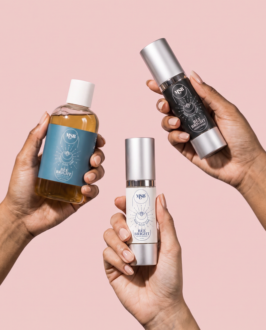 Three hands holding cosmetic bottles from the brand NPS against a solid pale pink background. The products include a clear bottle with amber liquid and a blue label, a black bottle with a silver cap and black label, and a white bottle with a silver cap and white label.